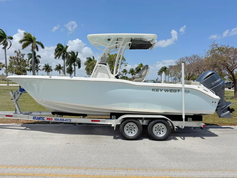 Slide: The Image of 2023 Key West 239 FS boat on trailer, parked near palm trees under a clear blue sky. - 0