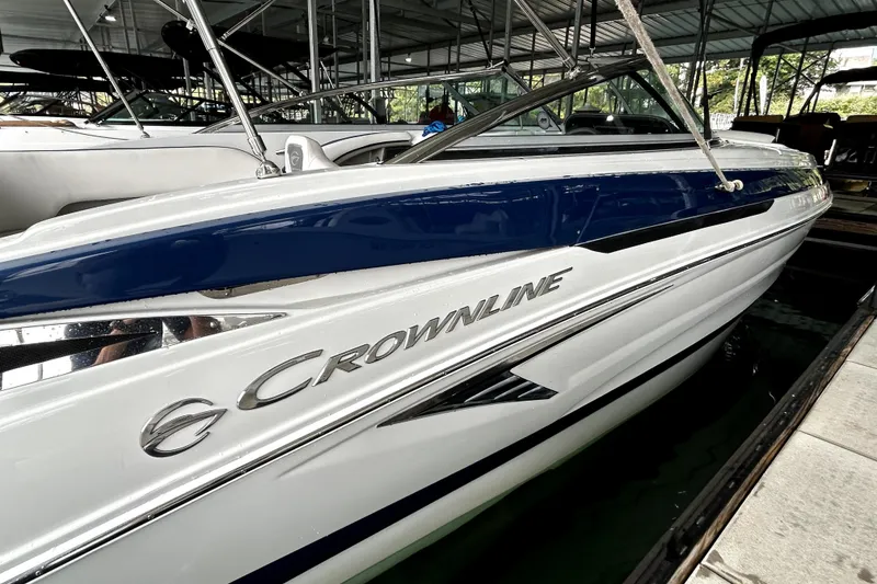 Slide: The Image of 2023 Crownline 260 XSS boat in marina, sleek design with blue and white exterior. - 18