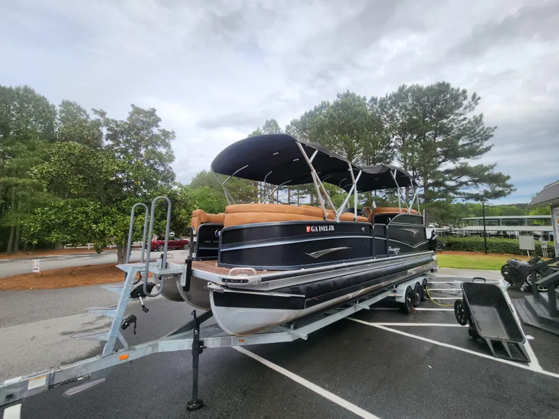Slide: The Image of 2021 Premier 290 Grand View pontoon boat on trailer, parked outdoors with trees in background. - 0