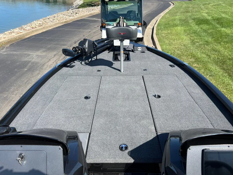 Slide: The Image of 2025 Vexus AVX1985S boat deck with gray carpeting, parked near a lake and grassy area. - 15