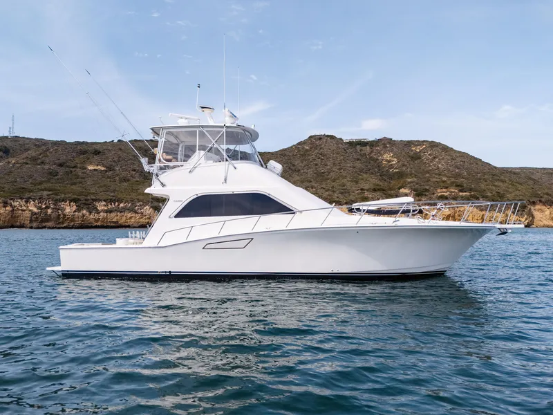 Slide: The Image of 2004 Cabo 48 Flybridge yacht on calm water with scenic hillside backdrop. - 1