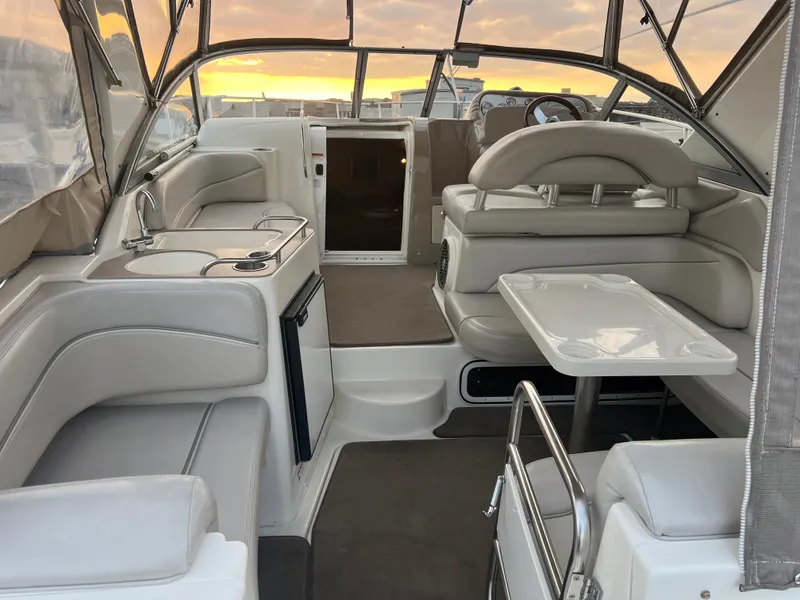 Slide: The Image of 2007 Larson Cabrio 330 boat interior with seating, table, and kitchenette at sunset. - 21