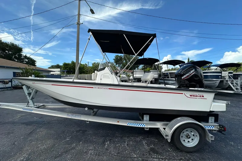 The Image of 2022 Boston Whaler 170 Montauk boat on trailer, featuring a Mercury outboard motor. - 0