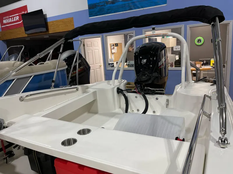 Slide: The Image of 2025 Boston Whaler 160 Super Sport boat interior with motor, showcased in a showroom. - 2