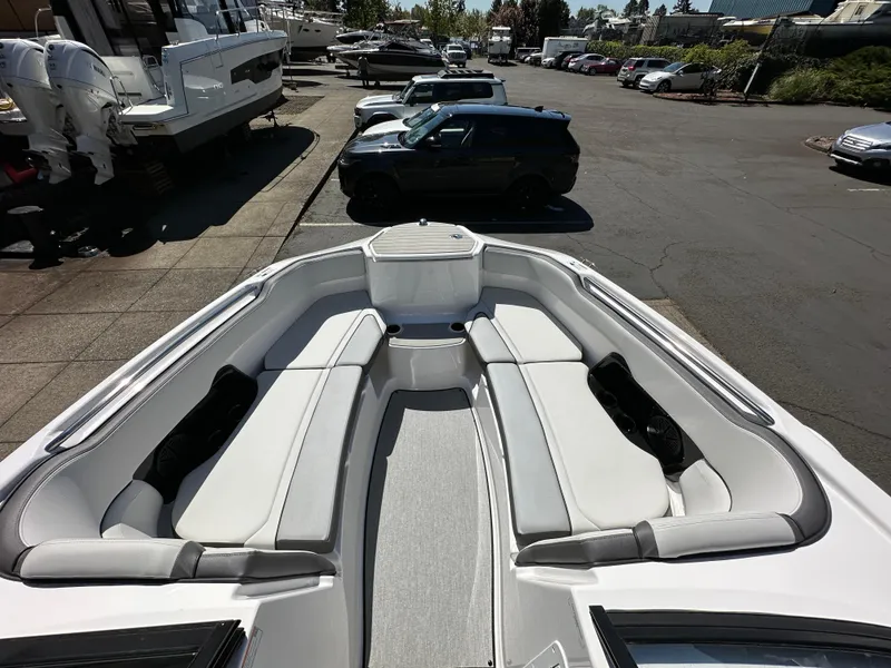Slide: The Image of 2024 Yamaha Boats AR250 bow seating area with sleek white upholstery in a marina setting. - 20