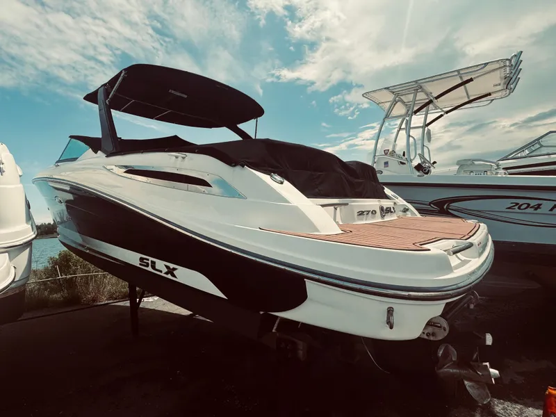 Slide: The Image of 2015 Sea Ray 270 SLX boat with black canopy, docked under a partly cloudy sky. - 14