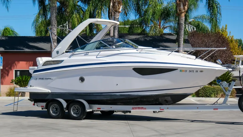 Slide: The Image of 2013 Regal 28 Express boat on trailer, parked outdoors with palm trees in background. - 1