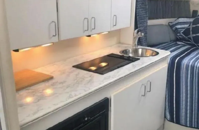 Slide: The Image of 1995 Wellcraft 330 Coastal interior with kitchenette, featuring stove, sink, and cozy sleeping area. - 28