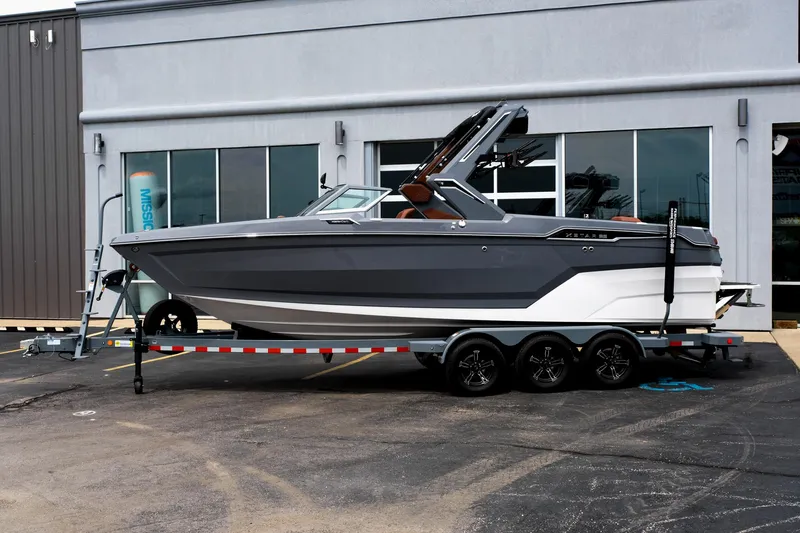 Slide: The Image of 2025 MasterCraft XStar 25 boat on trailer, parked outside a building. - 2