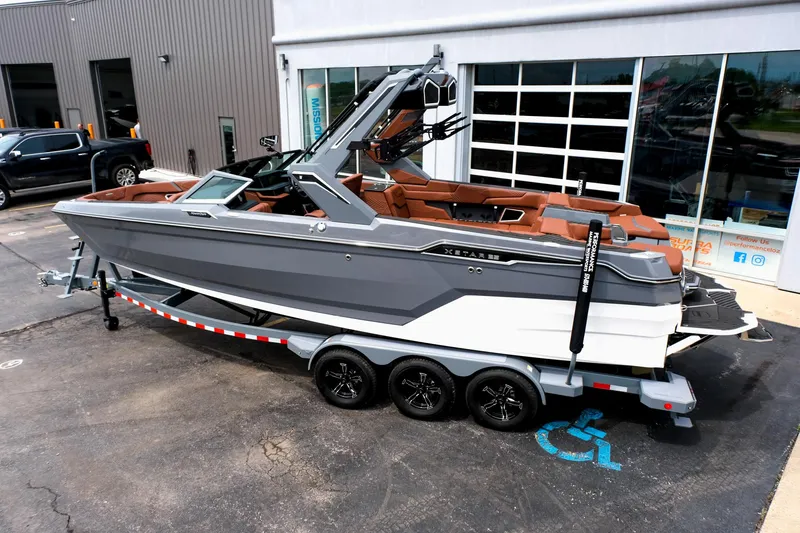Slide: The Image of 2025 MasterCraft XStar 25 boat on trailer, gray and brown design, parked outside a building. - 4