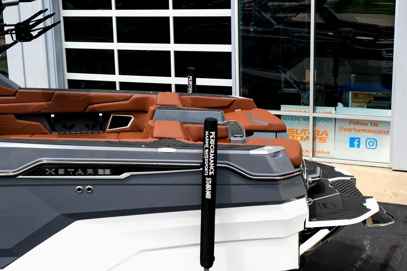 Slide: The Image of 2025 MasterCraft XStar 25 boat with brown seating, docked near a glass building. - 5