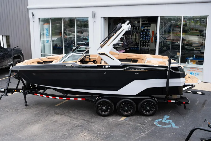 Slide: The Image of 2025 MasterCraft XStar 23 boat on trailer, black and white design, parked outside showroom. - 3