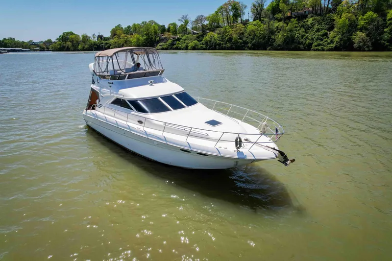 Slide: The Image of 1998 Sea Ray 400 Sedan Bridge yacht cruising on a calm river with lush green shoreline. - 9