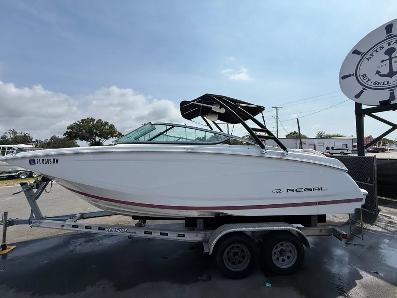 Slide: The Image of 2017 Regal 22 FasDeck boat on trailer, white with black canopy, parked outdoors. - 12