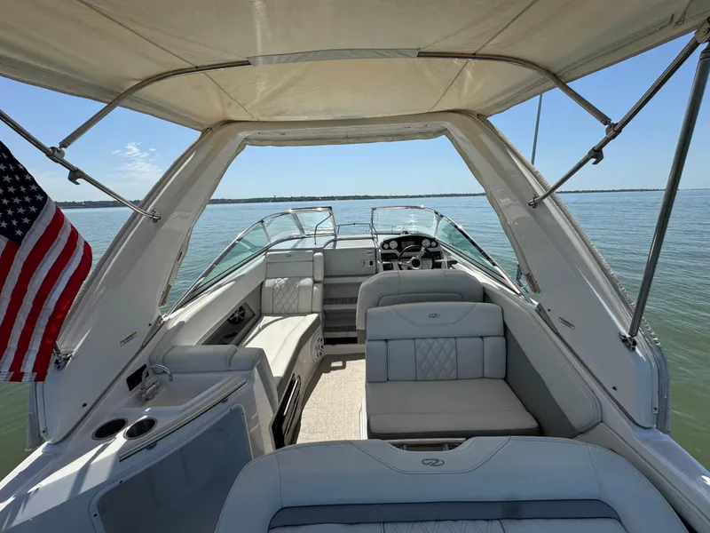 Slide: The Image of 2020 Regal 28 Express boat interior with seating, canopy, and American flag on calm water. - 26