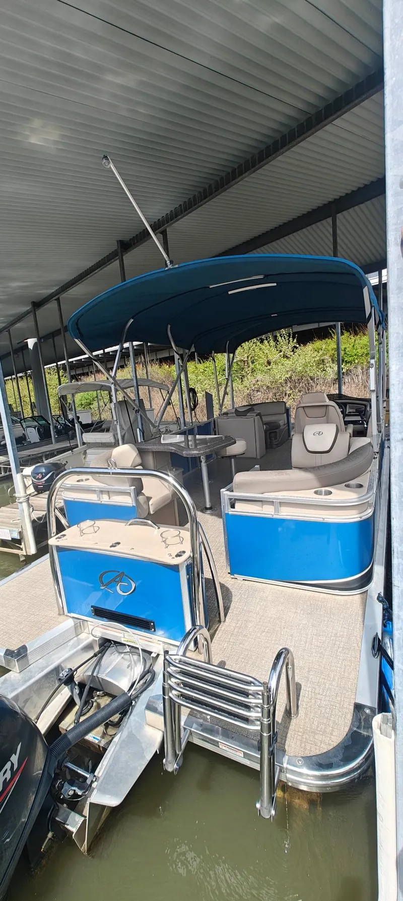 Slide: The Image of 2023 Avalon LSZ Entertainer pontoon boat with blue canopy and seating under a dock. - 4