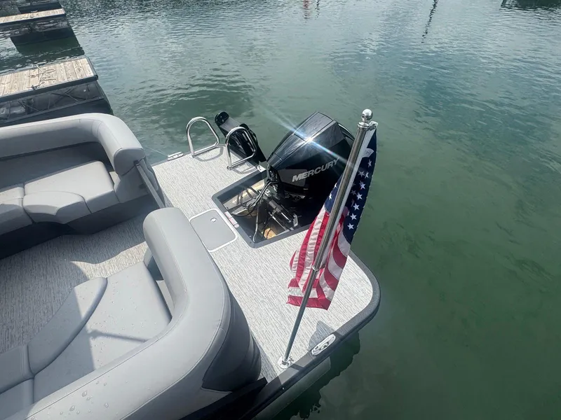 Slide: The Image of 2025 Bennington 22MFB pontoon boat with Mercury engine and American flag on calm water. - 31