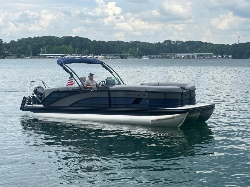 Slide: The Image of 2025 Bennington 24MFB pontoon boat on a serene lake with a cloudy sky backdrop. - 14