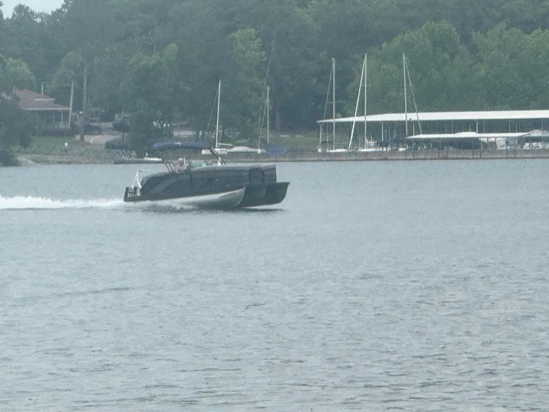 Slide: The Image of 2025 Bennington 24MFB pontoon boat cruising on a lake near a marina. - 17