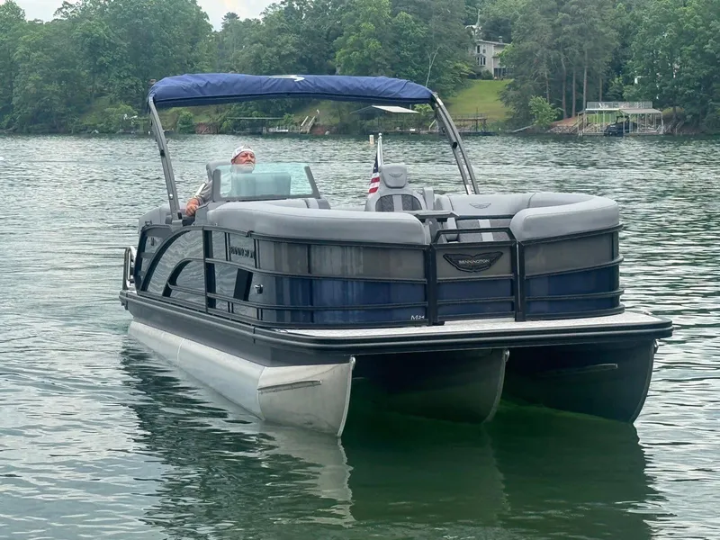 Slide: The Image of 2025 Bennington 24MFB pontoon boat cruising on a serene lake with lush greenery. - 2