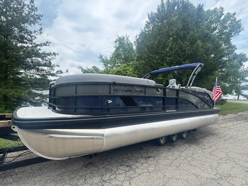 Slide: The Image of 2025 Bennington 24MFB pontoon boat on trailer, surrounded by trees and lake view. - 22