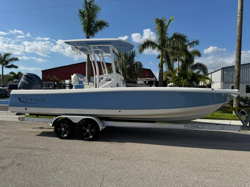 The Image of 2023 Robalo 246 Cayman boat on trailer, parked near palm trees under a clear sky. - 0