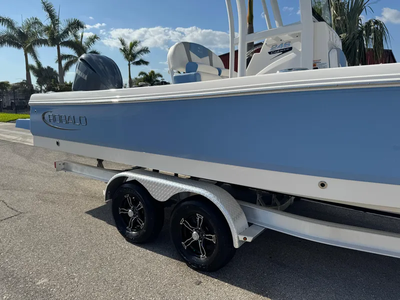 Slide: The Image of 2023 Robalo 246 Cayman boat on trailer, light blue hull, palm trees in background. - 27