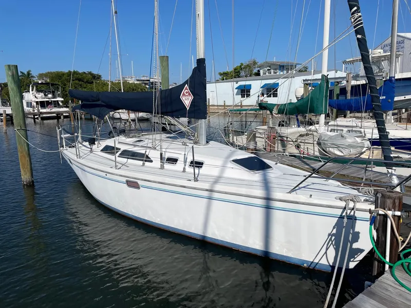 Slide: The Image of 1997 Catalina 320 sailboat docked at marina, featuring sleek white hull and blue sail cover. - 0