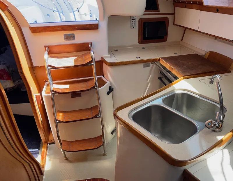 Slide: The Image of Interior of a 1997 Catalina 320 sailboat featuring a compact kitchen with a sink and wooden accents. - 11