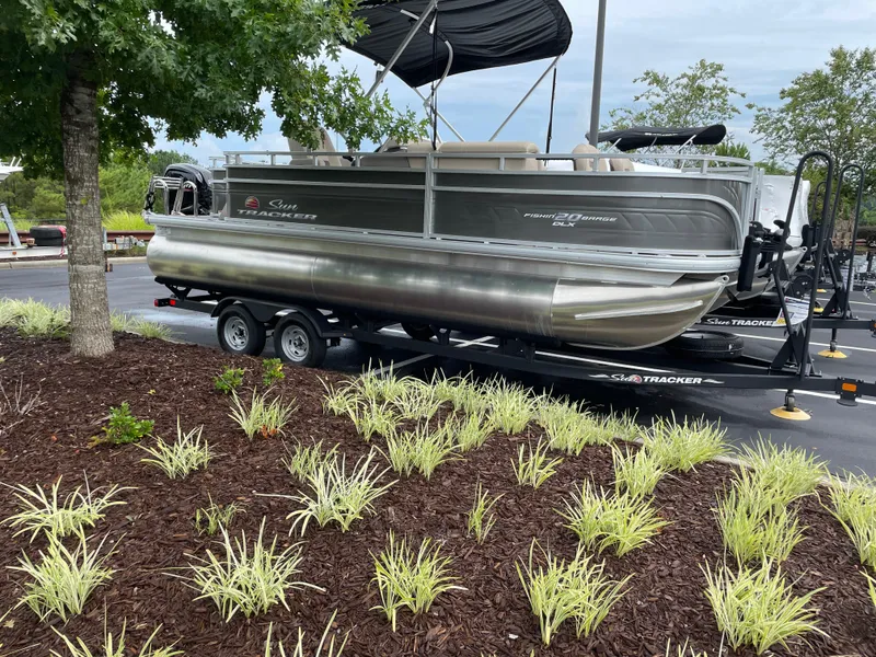 The Image of 2025 Sun Tracker Fishin' Barge 20 DLX pontoon boat on trailer, parked near landscaped area. - 0