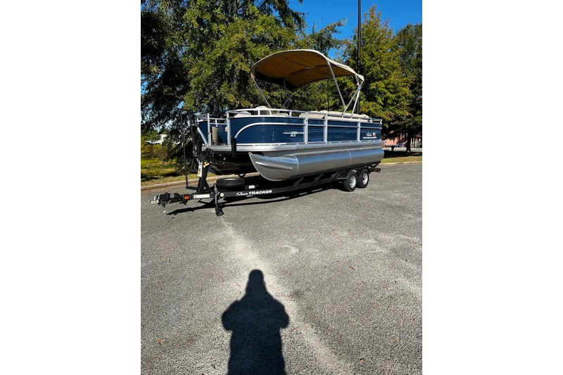 The Image of 2025 Sun Tracker Fishin' Barge 20 DLX pontoon boat on trailer, parked outdoors. - 0