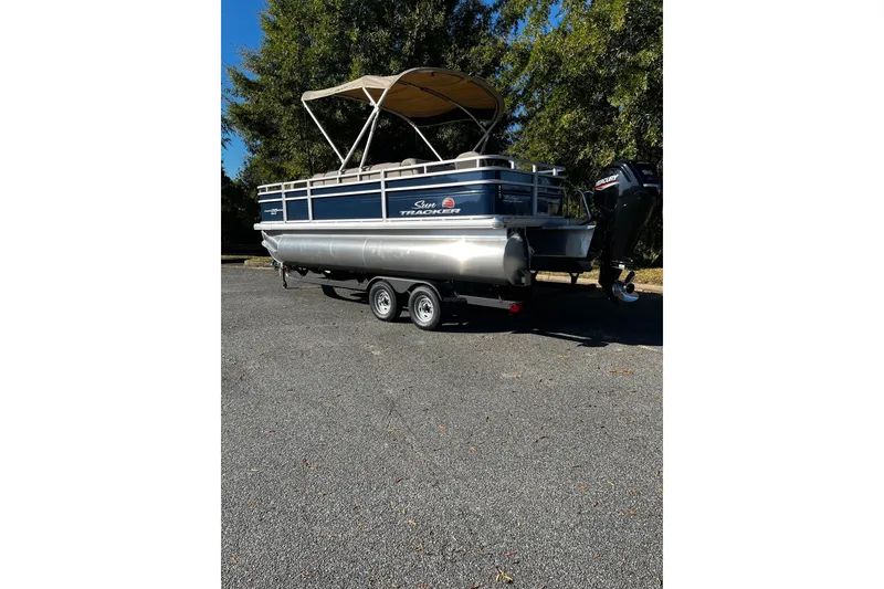 Slide: The Image of 2025 Sun Tracker Fishin' Barge 20 DLX pontoon boat on trailer, parked outdoors. - 2