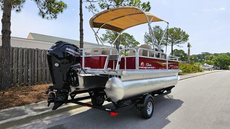 Slide: The Image of 2025 Sun Tracker Bass Buggy 18 DLX pontoon boat on trailer, parked on a sunny street. - 2