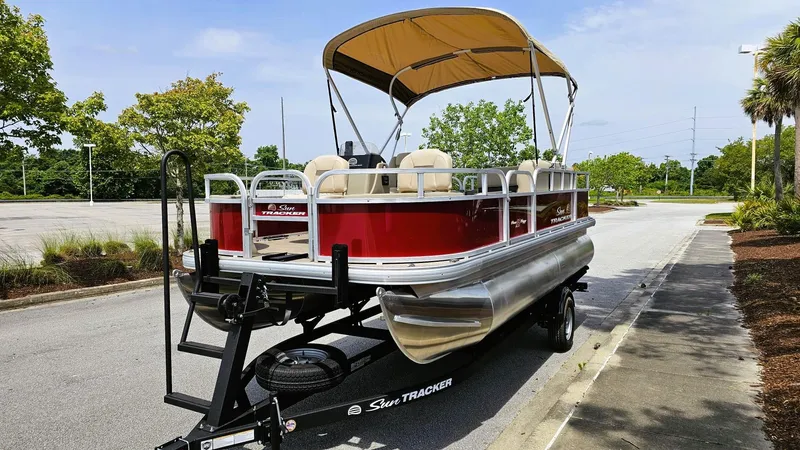 Slide: The Image of 2025 Sun Tracker Bass Buggy 18 DLX pontoon boat on trailer, parked outdoors. - 4
