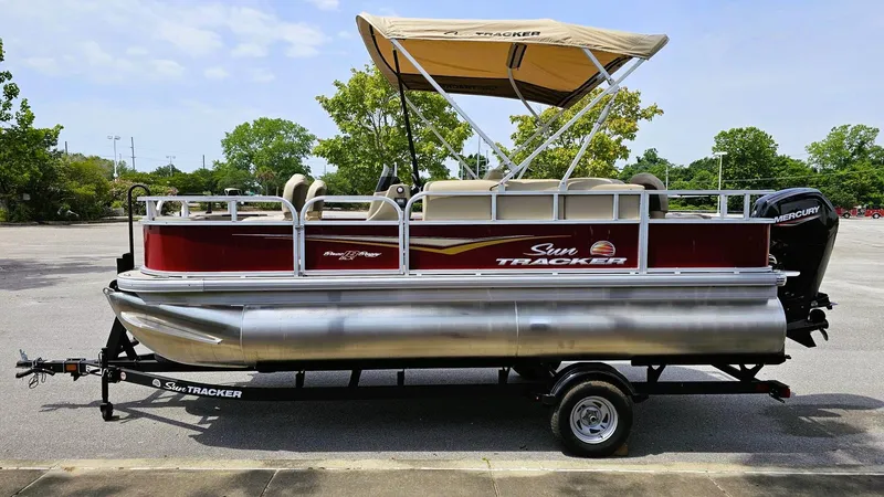 Slide: The Image of 2025 Sun Tracker Bass Buggy 18 DLX pontoon boat on trailer, parked outdoors. - 5