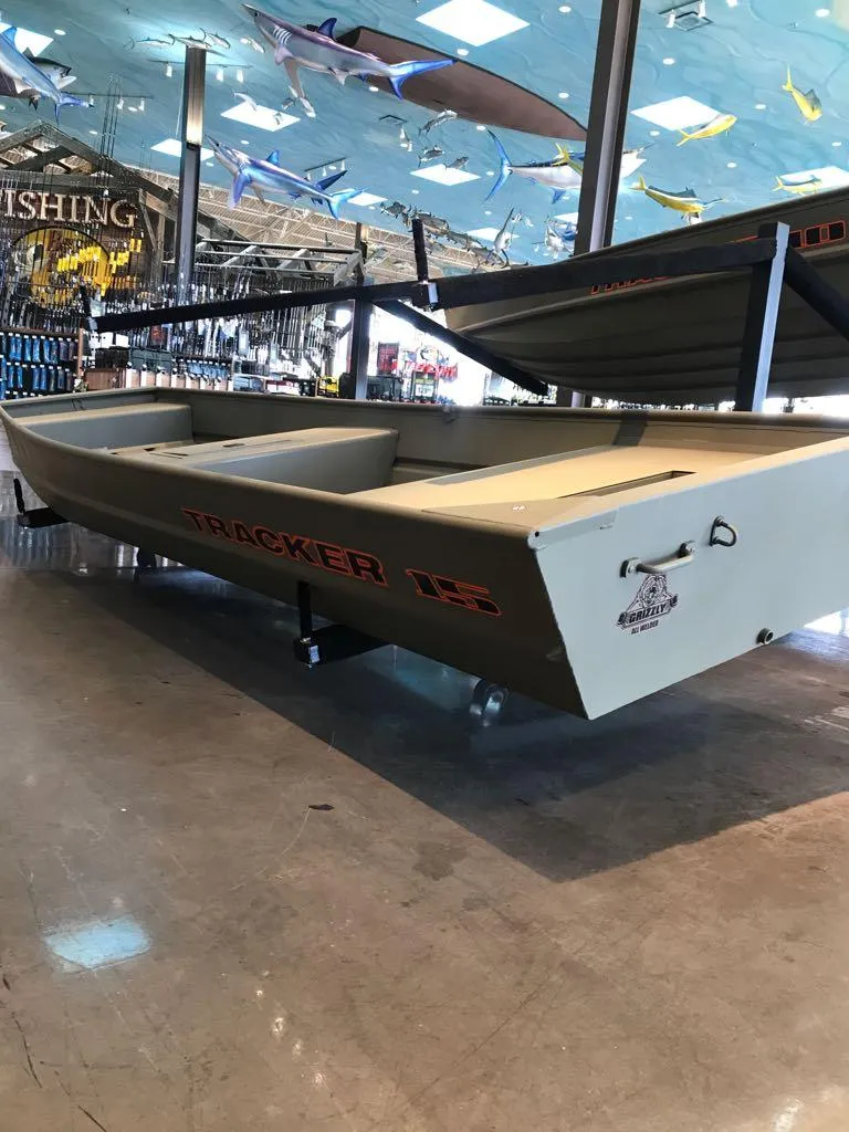 Slide: The Image of 2025 Tracker Grizzly 15 Jon boat displayed in a showroom with fishing gear. - 4