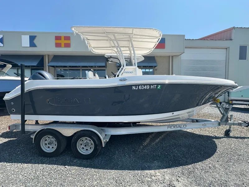 Slide: The Image of 2023 Robalo R200 Center Console boat on trailer, parked outside a building. - 0