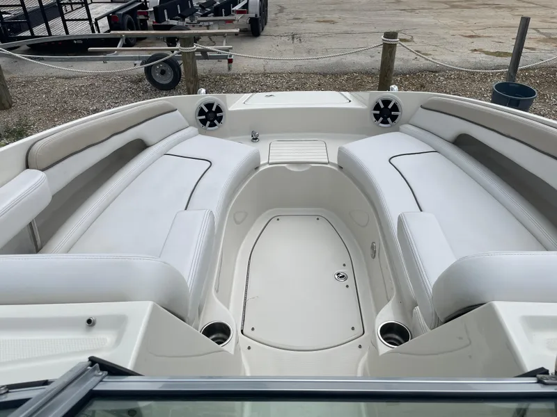 Slide: The Image of 2009 Sea Ray 260 Sundeck interior with white seating and speakers, docked on gravel. - 19