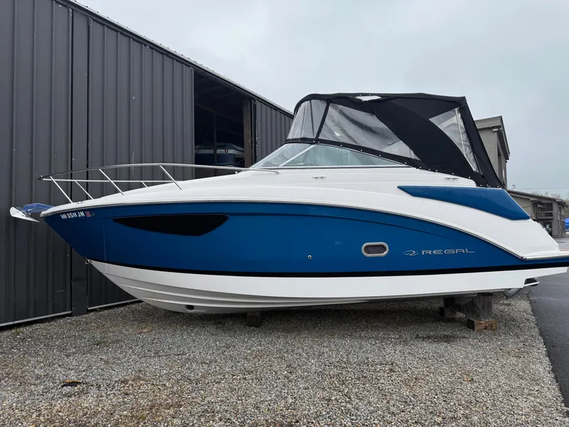 Slide: The Image of 2019 Regal 26 Express boat with blue hull, docked near a metal building. - 0