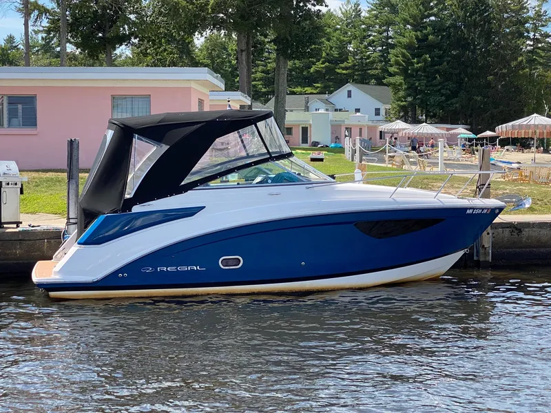 Slide: The Image of 2019 Regal 26 Express boat docked by a lakeside with trees and houses in the background. - 1