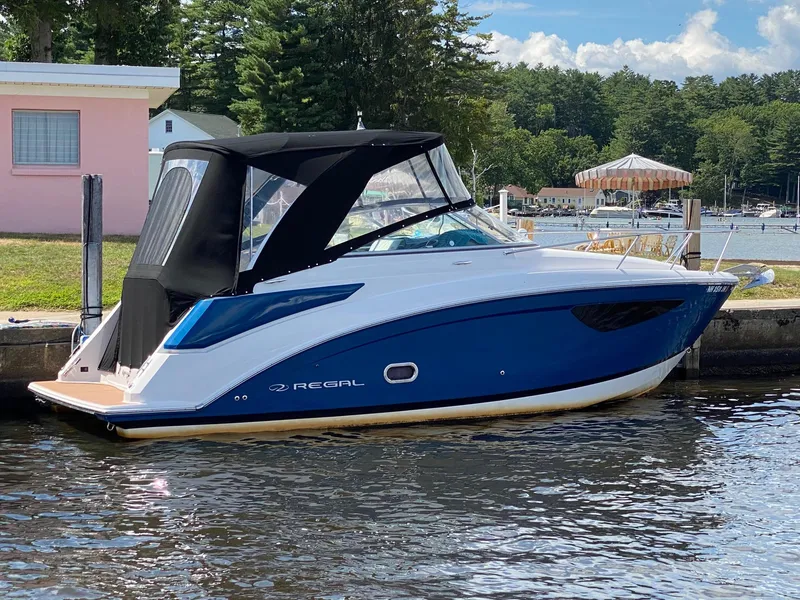 Slide: The Image of 2019 Regal 26 Express boat docked by a lakeside, featuring a sleek blue and white design. - 2
