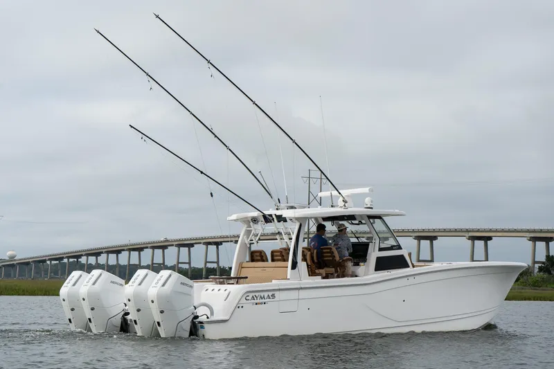 Slide: The Image of 2025 Caymas 44 CT boat with multiple fishing rods, cruising on water near a bridge. - 1