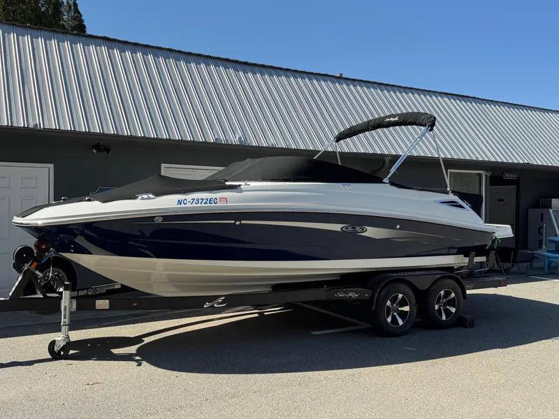 Slide: The Image of 2015 Sea Ray 220 Sundeck boat on trailer, parked outside a building. - 1