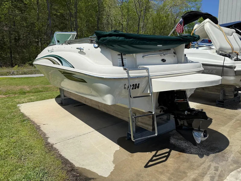 Slide: The Image of 2001 Sea Ray 210 SD boat with green cover, parked on concrete, surrounded by trees. - 1