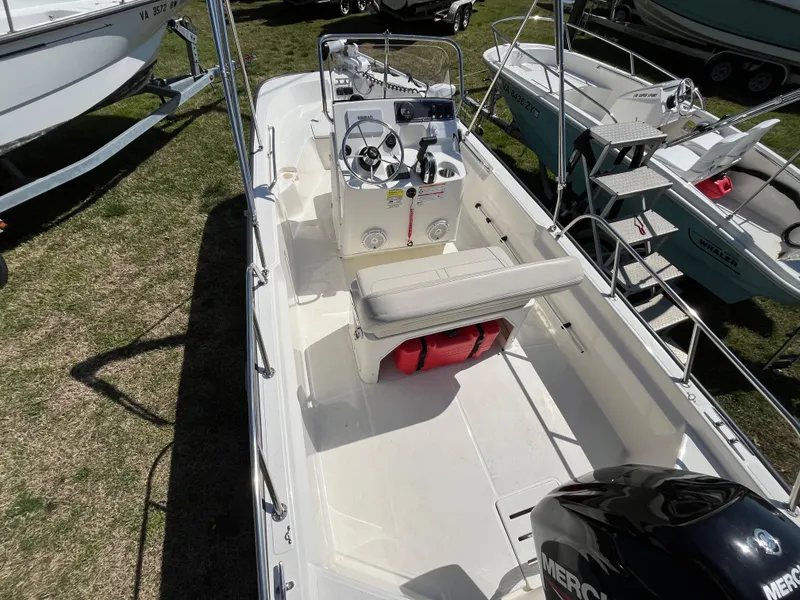 Slide: The Image of 2024 Boston Whaler 150 Montauk boat with seating and control console, displayed outdoors. - 2