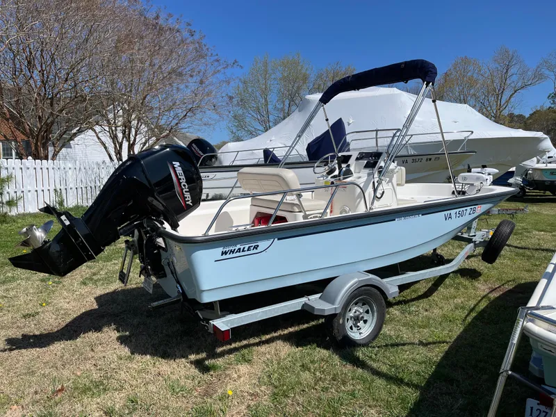 Slide: The Image of 2024 Boston Whaler 150 Montauk boat on trailer, parked on grass, with Mercury outboard motor. - 20