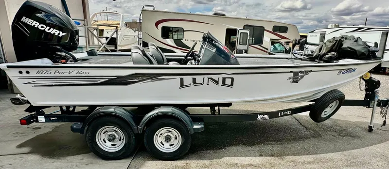 Slide: The Image of 2018 Lund 1875 Pro-V Bass boat on trailer, parked near RVs. - 6