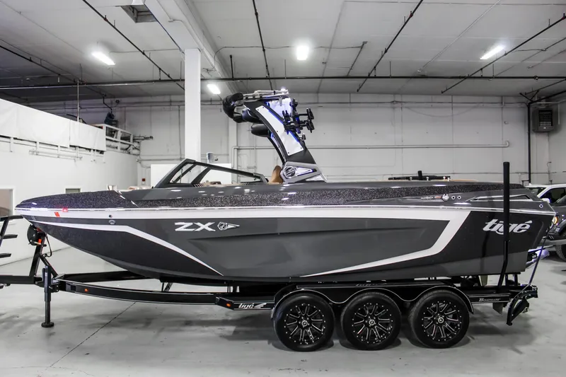 Slide: The Image of 2021 Tigé 25ZX boat in a showroom, featuring sleek design and triple-axle trailer. - 2