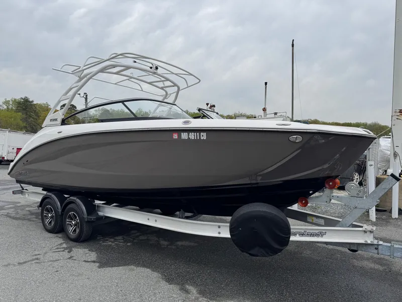 Slide: The Image of 2023 Yamaha Boats 252SE on trailer, sleek design, gray hull, white accents, outdoor setting. - 0