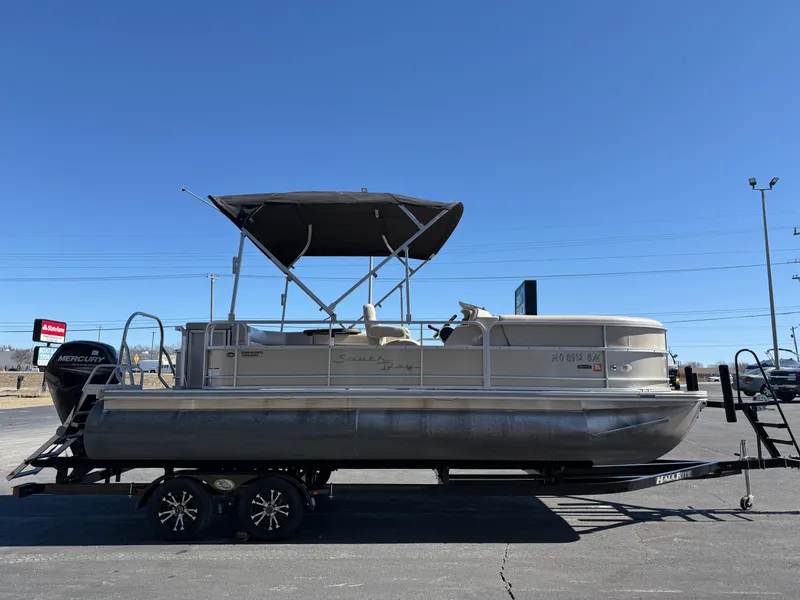 Slide: The Image of 2019 South Bay 222CR pontoon boat on trailer, with canopy, parked outdoors. - 2